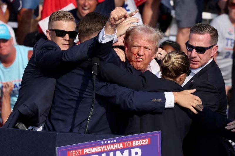 Mantan Presiden AS Donald Trump memberi isyarat dengan wajah berlumuran darah saat ia dibantu oleh personel Dinas Rahasia AS setelah ia ditembak di telinga kanannya saat kampanye di Butler Farm Show d