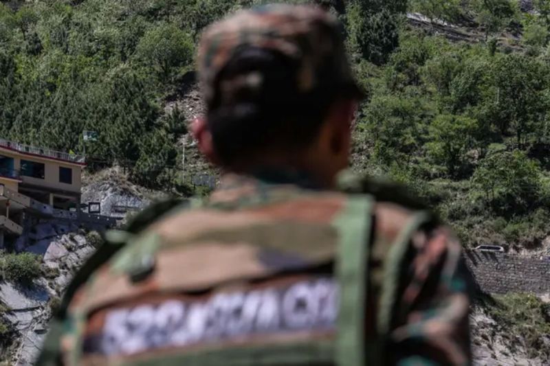 Bendera dan bangunan milik Pakistan dipantau seorang serdadu di wilayah Kashmir yang dikendalikan oleh India.(GETTY IMAGES via BBC INDONESIA)