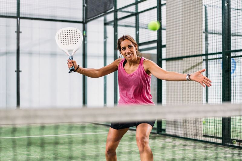 Seorang perempuan bermain padel di lapangan padel rumput hijau dalam ruangan.()