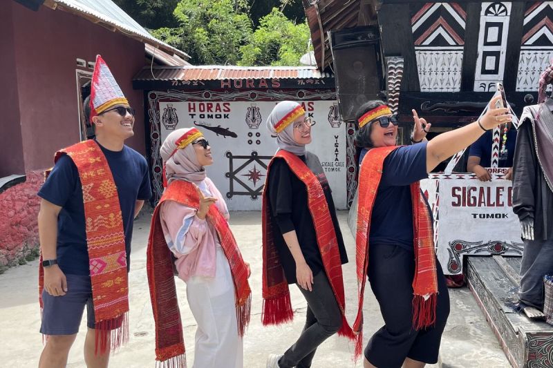 Wisatawan memakai ulos dan sortali sebelum ikut manortor di Sigale-gale, Desa Tomok, Kabupaten Samosir, Sumatera Utara, Jumat (16/5/2025). (Kompas.com/ Suci Wulandari Putri)