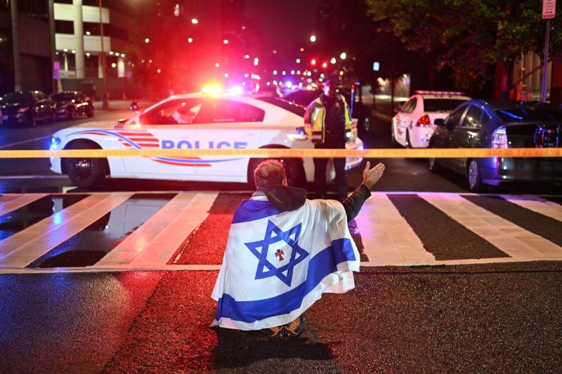 Seorang pria memakai bendera Israel duduk di tengah jalan lokasi penembakan di Museum Yahudi Washington DC, Amerika Serikat, Kamis (22/5/2025)