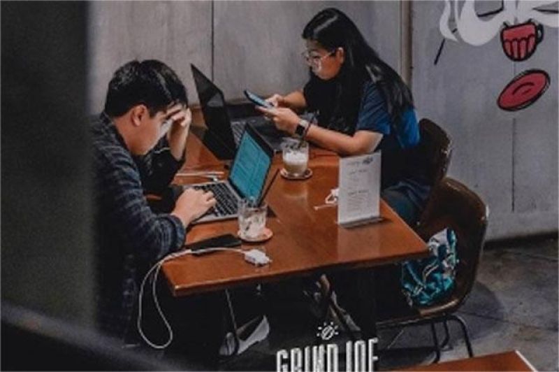anak muda bekerja di kafe dengan laptop, tampak sibuk tapi cemas soal pemasukan