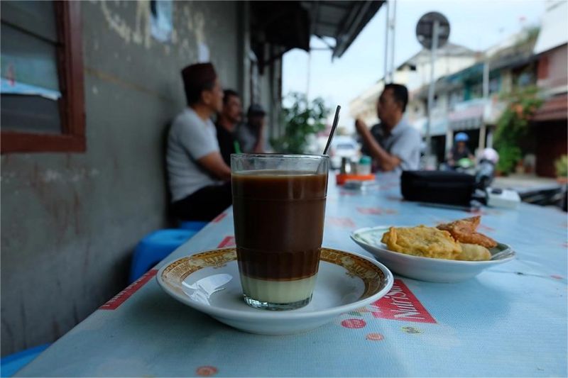 kedai kopi kecil di gang sempit dengan pelanggan muda duduk santai menikmati kopi