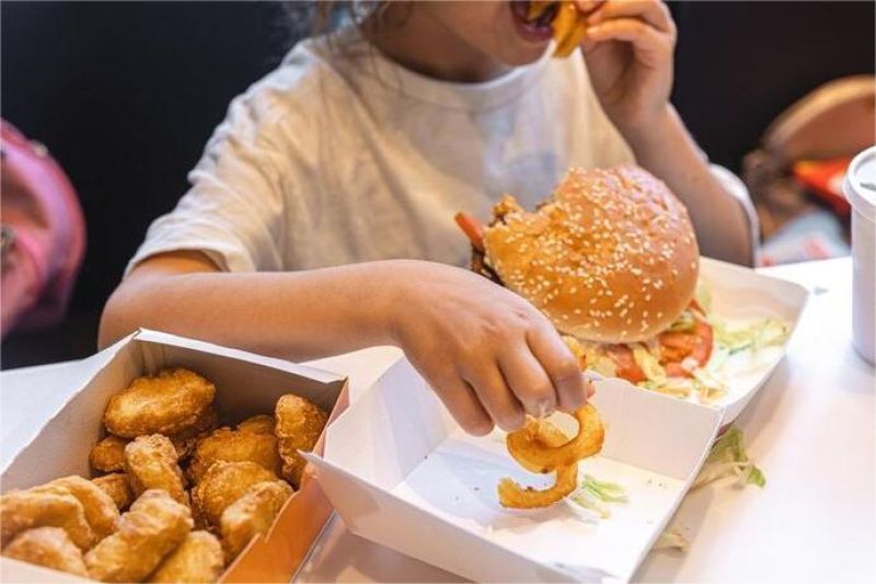 anak obesitas duduk sambil makan makanan cepat saji