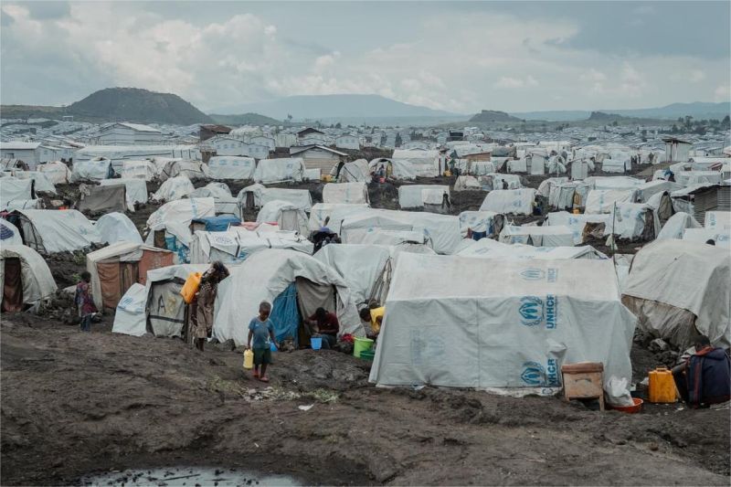 pengungsi berjalan di kamp pengungsian dengan latar belakang tenda darurat