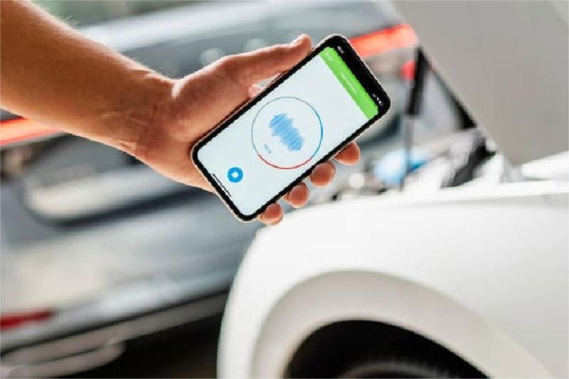 teknisi memegang smartphone dengan aplikasi AI deteksi suara mesin di pabrik