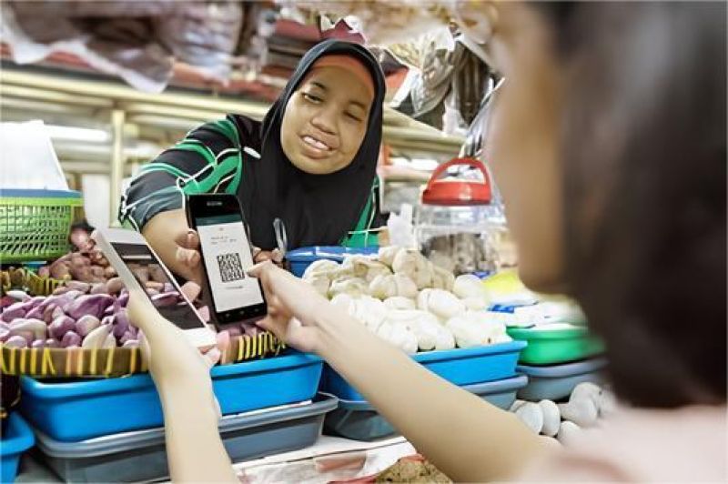 pelaku UMKM memegang smartphone sambil melayani pelanggan di toko kecil