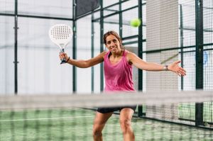Seorang perempuan bermain padel di lapangan padel rumput hijau dalam ruangan.()
