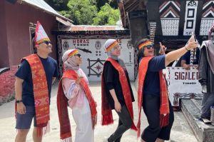 Wisatawan memakai ulos dan sortali sebelum ikut manortor di Sigale-gale, Desa Tomok, Kabupaten Samosir, Sumatera Utara, Jumat (16/5/2025). (Kompas.com/ Suci Wulandari Putri)