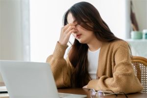 ilustrasi perempuan memijat mata lelah di depan laptop karena terlalu lama menatap layar
