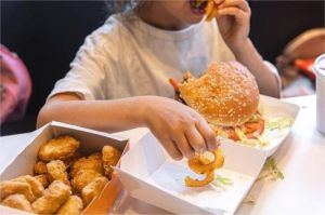 anak obesitas duduk sambil makan makanan cepat saji