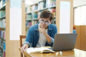 mahasiswa fokus belajar dengan laptop dan catatan di perpustakaan